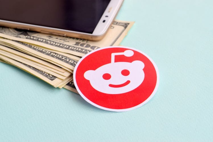 Stock graphic with a smartphone, dollar bills and a Reddit logo.