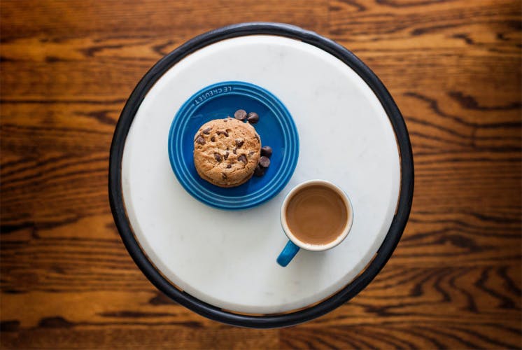 cookie on plate with cup of coffee on table aerial view