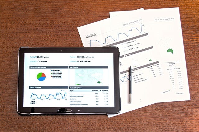 Stock image of tablet with analytics on the screen and two paper documents next to it.