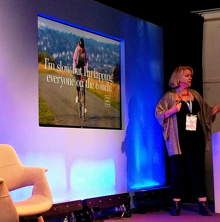 Kate Dale stands in front of a projector screen showing one of the iconic images from the first wave of the campaign