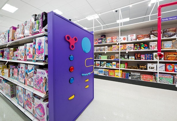 A photograph of Target's reimagined toy store, with a large purple board at the end of one aisle that has embedded buttons, handles and things to spin and move around.