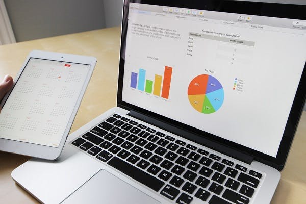 Stock image of laptop showing graphs on screen and next to it, a hand holding a tablet.