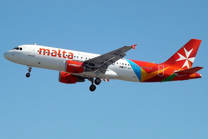 An Air Malta-branded aeroplane flies through a blue sky.