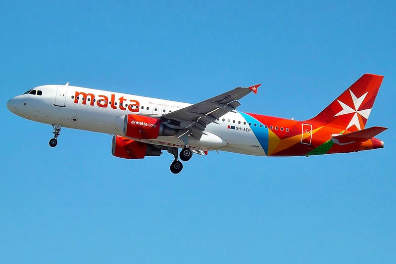 An Air Malta-branded aeroplane flies through a blue sky.