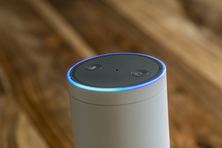 White Amazon Echo Plus activated recognition system photographed on wooden table in living room.