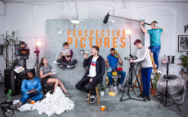 A group of young people striking poses in a studio with the words 'Perspective Pictures' overlaid on the backdrop. Rupert Rixon sits in the middle holding a megaphone.