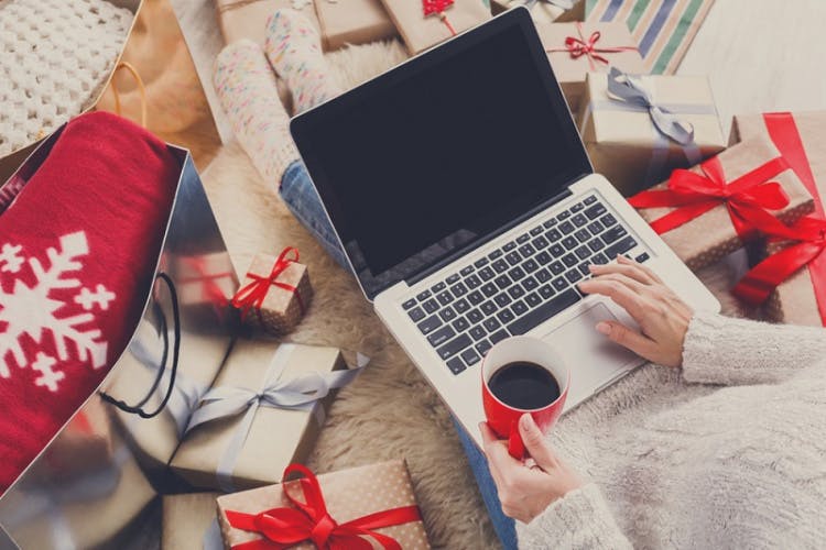 Person browsing on a laptop surrounded by winter holiday gifts