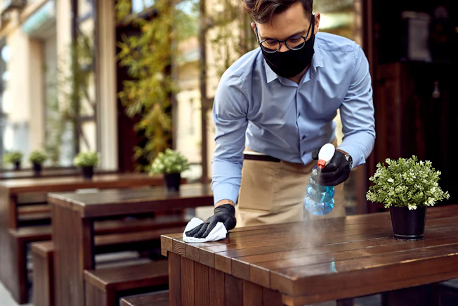 man in mask cleaning restaurant table