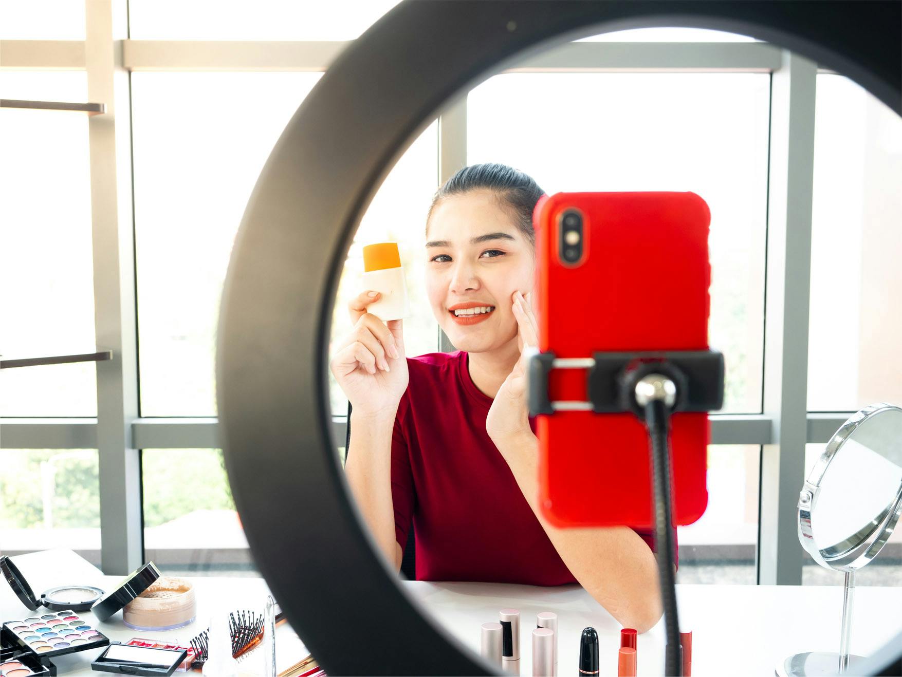 Female beauty influencer demonstrating product on livestream filming on mobile phone with light ring