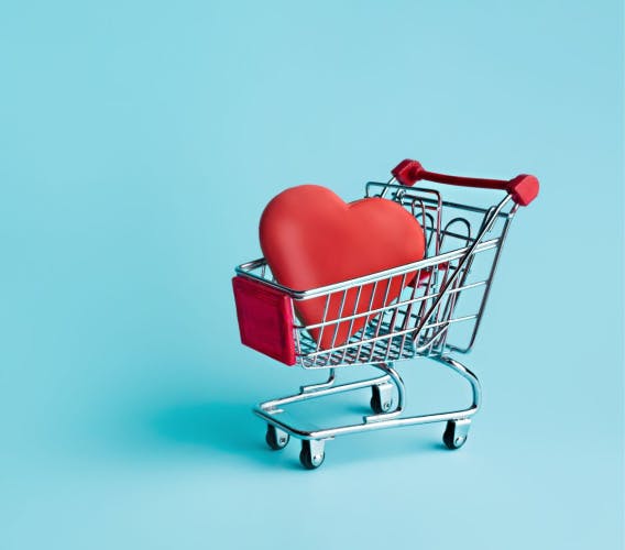 miniature shopping trolley containing large red heart figurine on a turquoise background