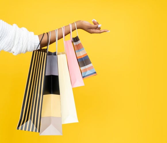 five shopping bags hanging from an arm with a white sleeve on a yellow background