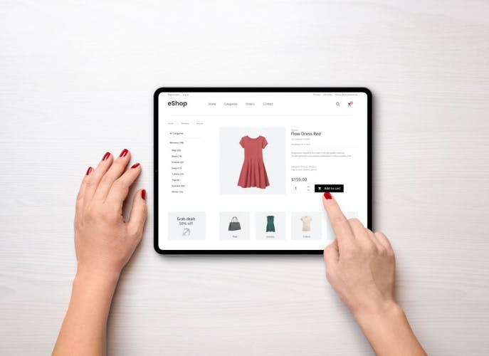a woman's hands interacting with a product page showing a red dress on a tablet screen upon a white background