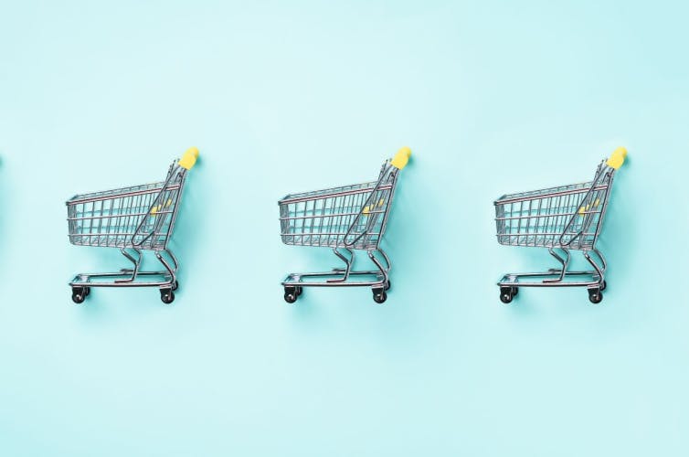 three miniature shopping trolleys placed sideways in a row on a light turquoise background