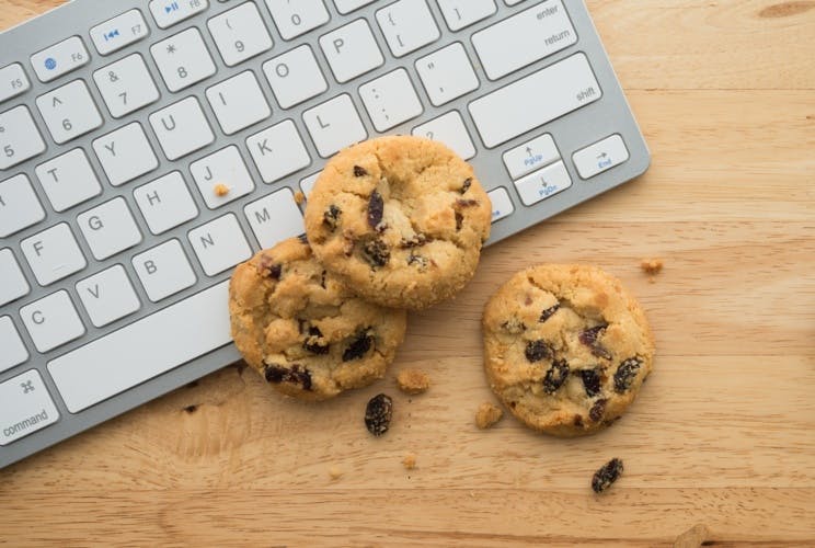 Three cookies with some crumbs resting against a Mac keyboard.