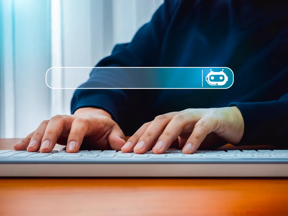 A pair of hands typing on a keyboard with a search bar above that has a robot icon at one end.