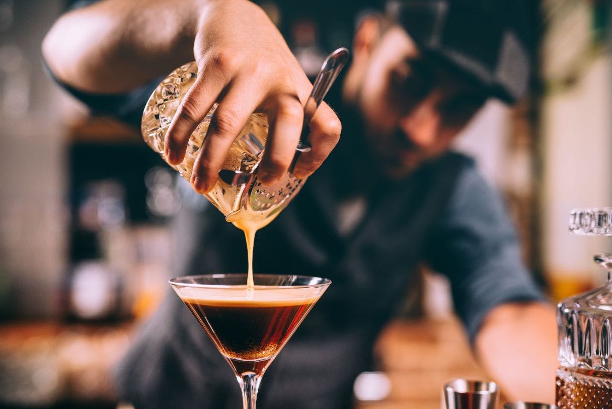 A barista pours a coffee-based cocktail from a shaker into a martini glass.